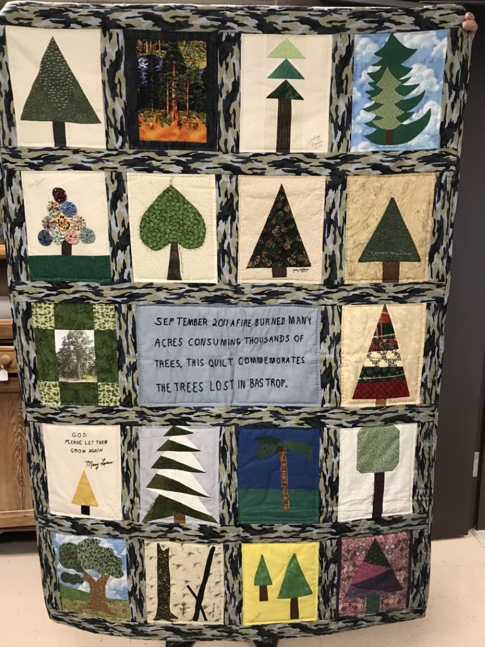 A quilt is shown with trees and dedicated to the Bastrop Complex Fire.
