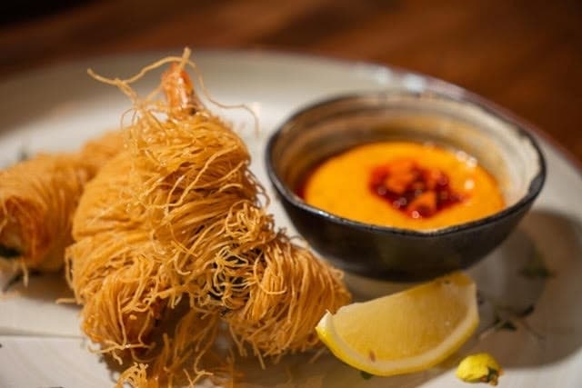 Fried food on a plate with a side of sauce and lemon wedge. 