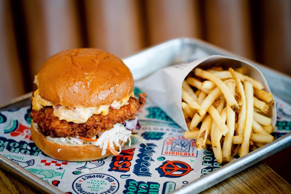 Chicken sandwich with a side of fries on a paper-line metal tray. 