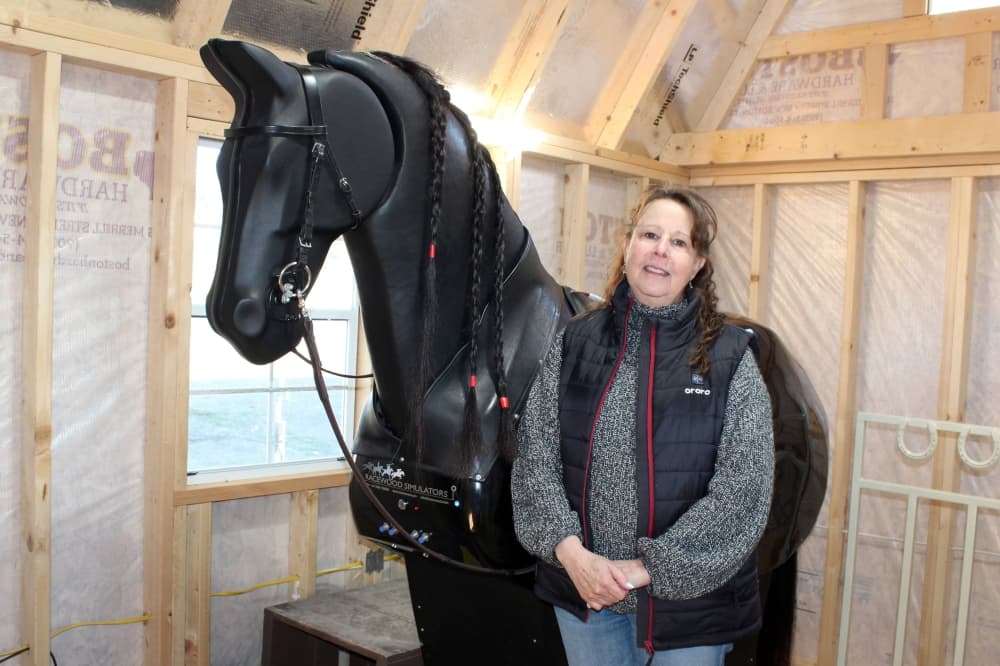 Female standing next to a life-size horse simulator.