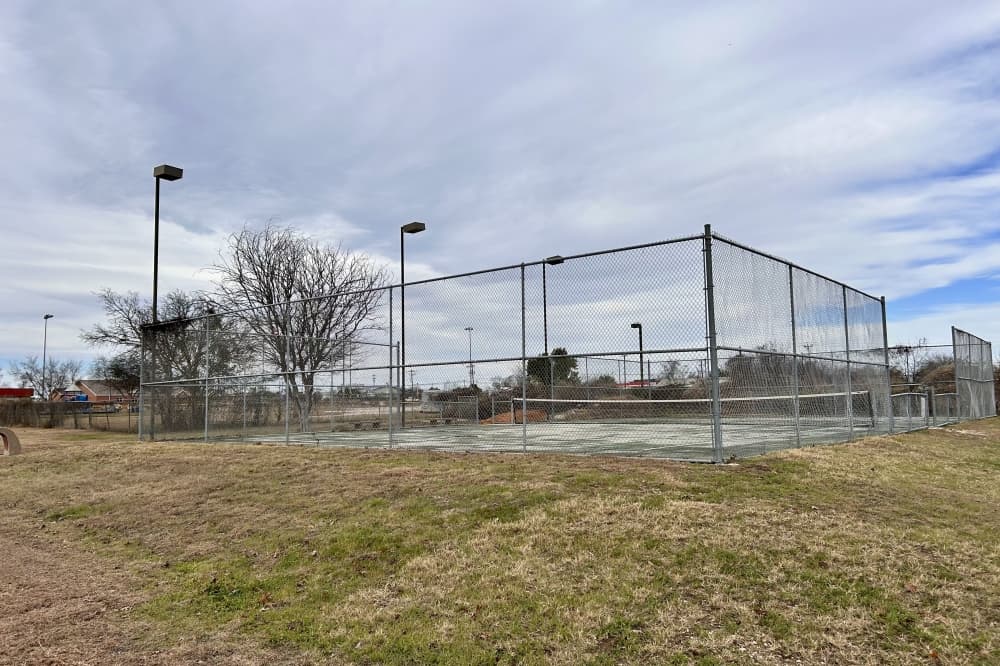 A photo of a tennis court outside with grass in front of it