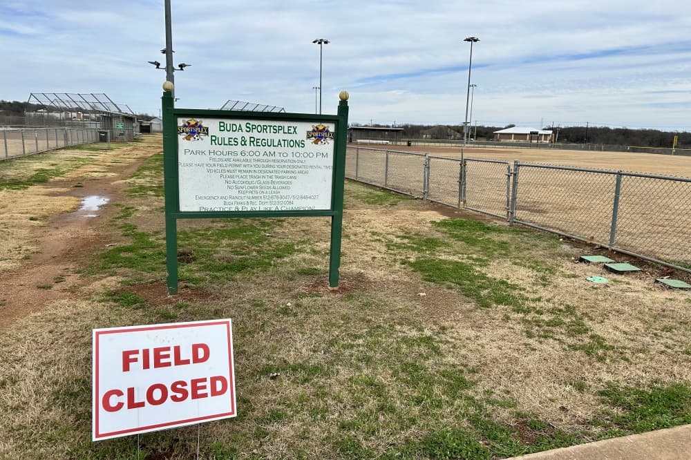 A picture of a sign that says "Buda Sportsplex" in front of softball fields, with another smaller sign that says "Field Closed"