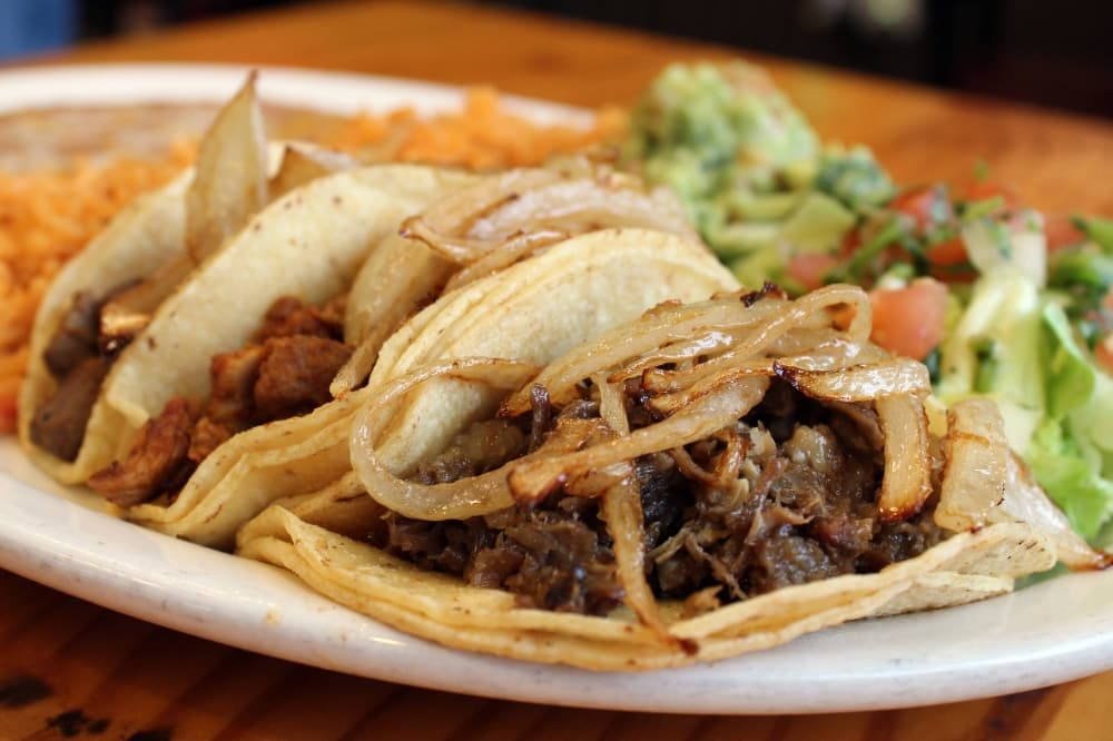 Three beef tacos on corn tortillas with side of beans, rice and salad. 