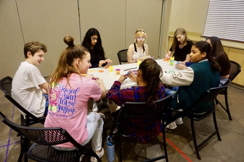 Group of teens engaging with one another around a table.