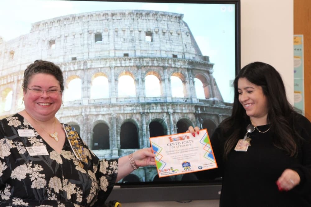 two women smile as they pass a certificate
