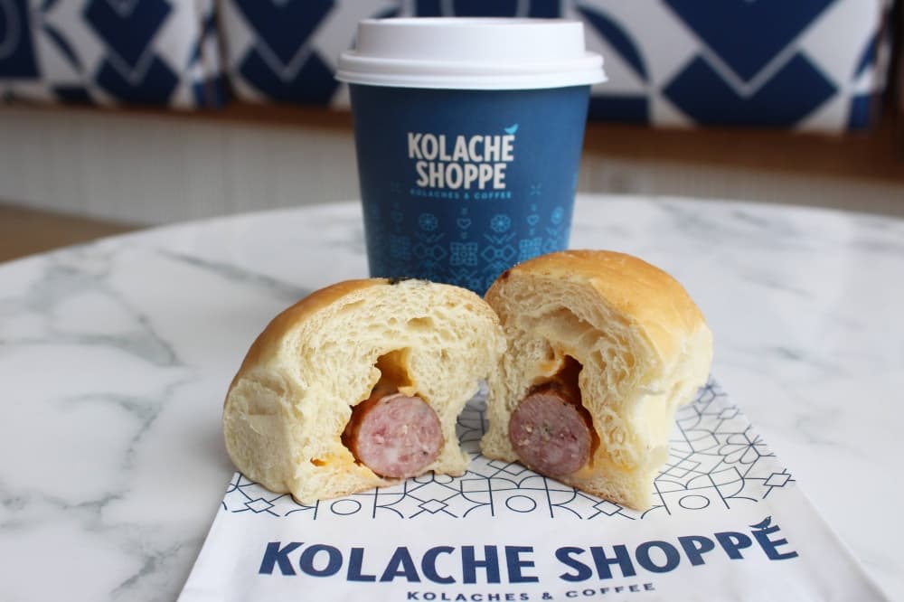 Side view of kolache with link sausage and cheese with a cup of coffee in the background. 