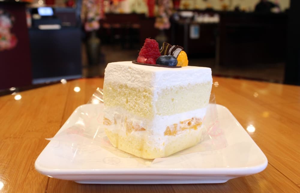 Slice of yellow cake with white frosting and topped with fruit and chocolate garnish. 