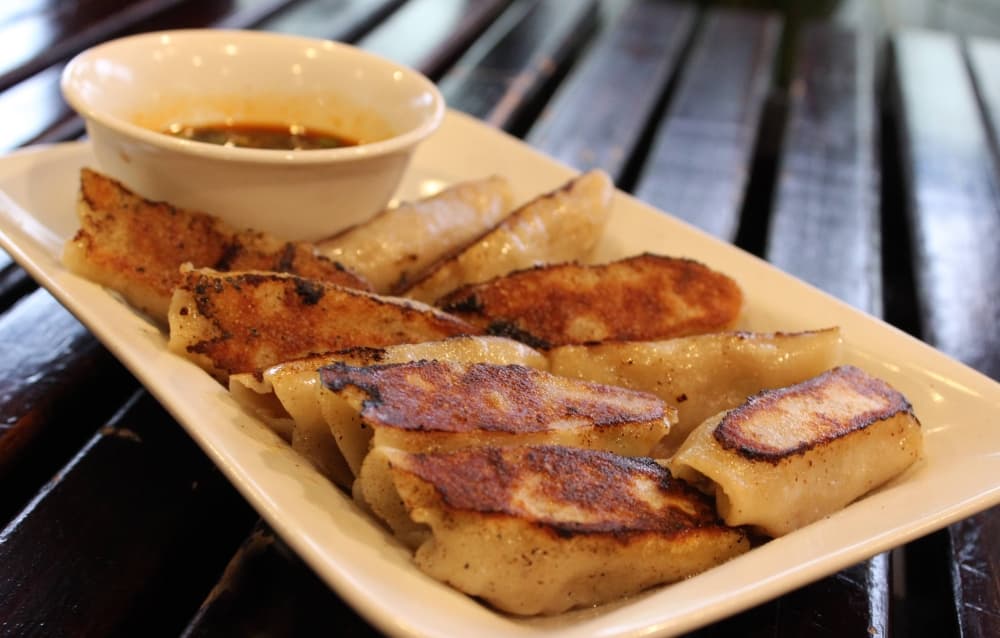 Plate of pot stickers and bowl of dipping sauce. 