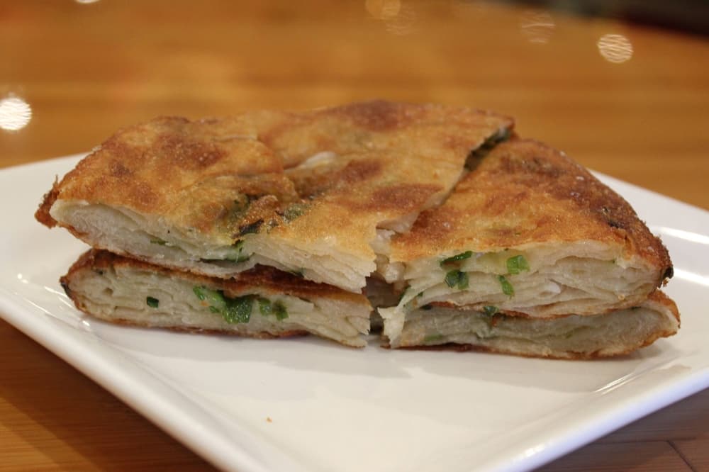 Green onion pancake quartered and stacked on a plate. 