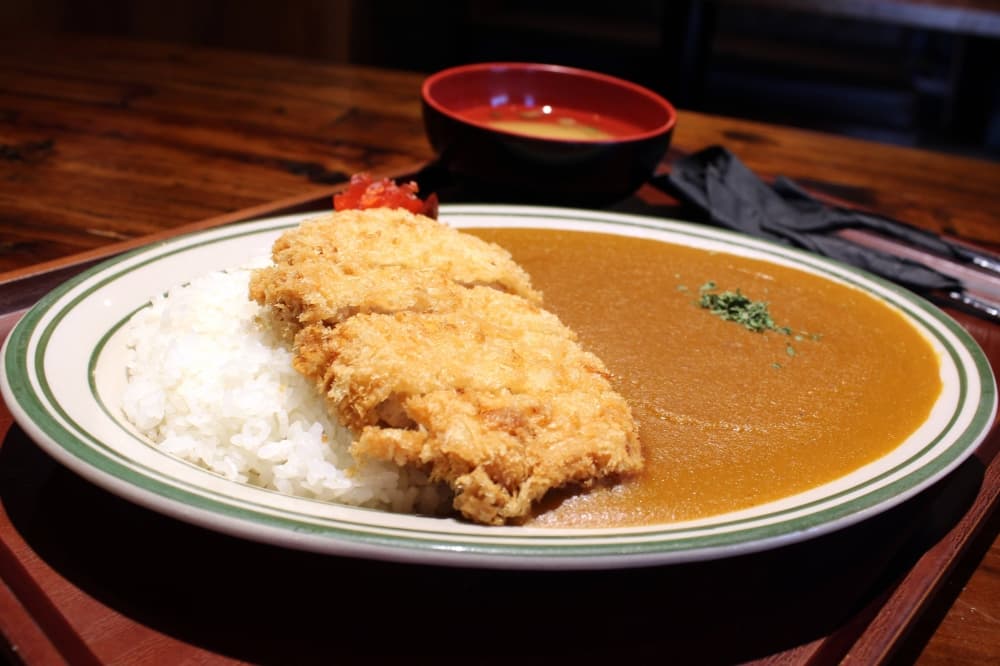 Chicken and rice next to a brown sauce on a plate. 