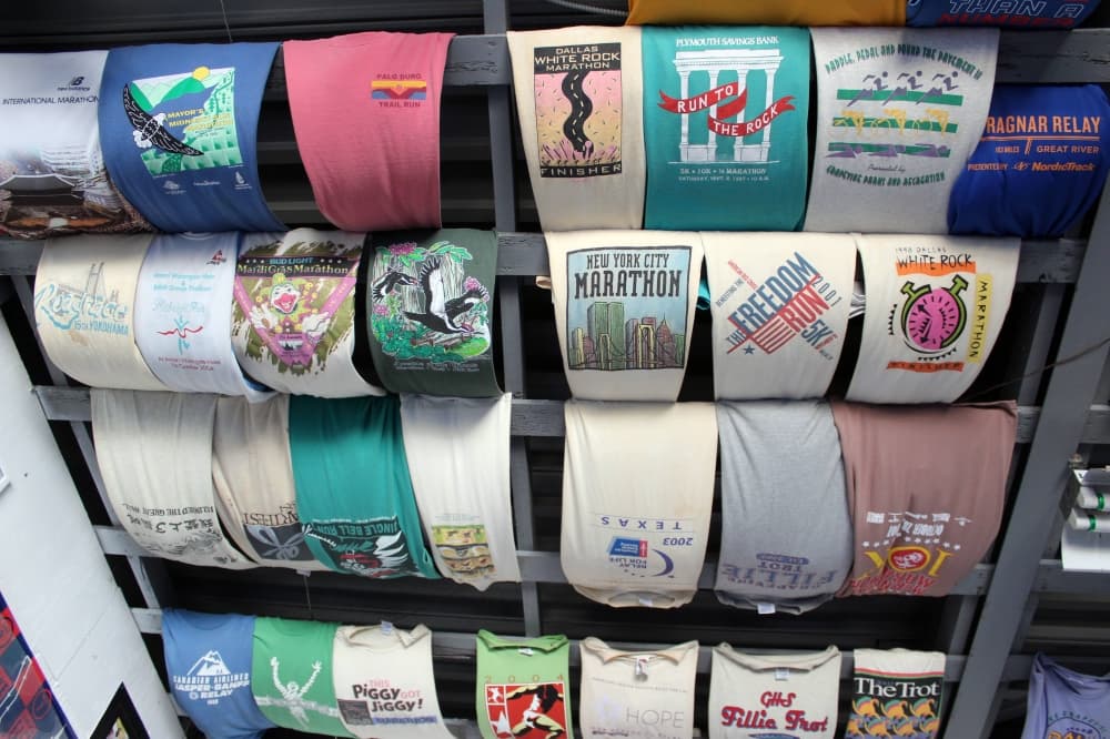 Marathon t-shirts from a variety of states hung side by side over a ceiling. 