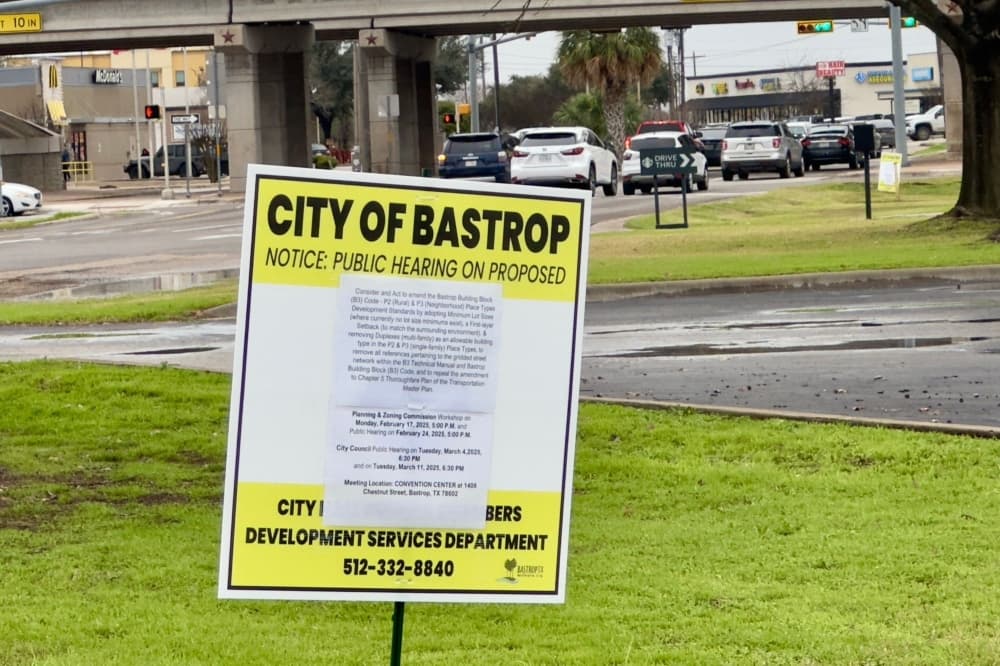 The yellow and white sign telling the public about the upcoming hearings is shown near HEB.