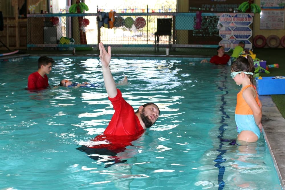 Young adult male demonstrating proper arm movement to a young female in a swimming pool. 