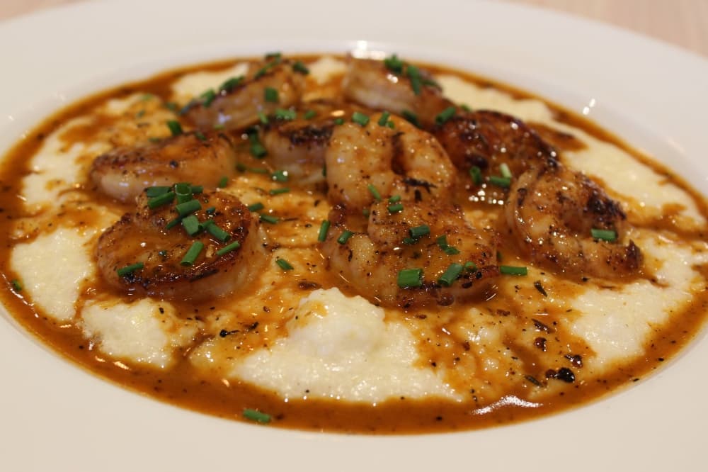 Shrimp and grits in a bowl topped with brown sauce.