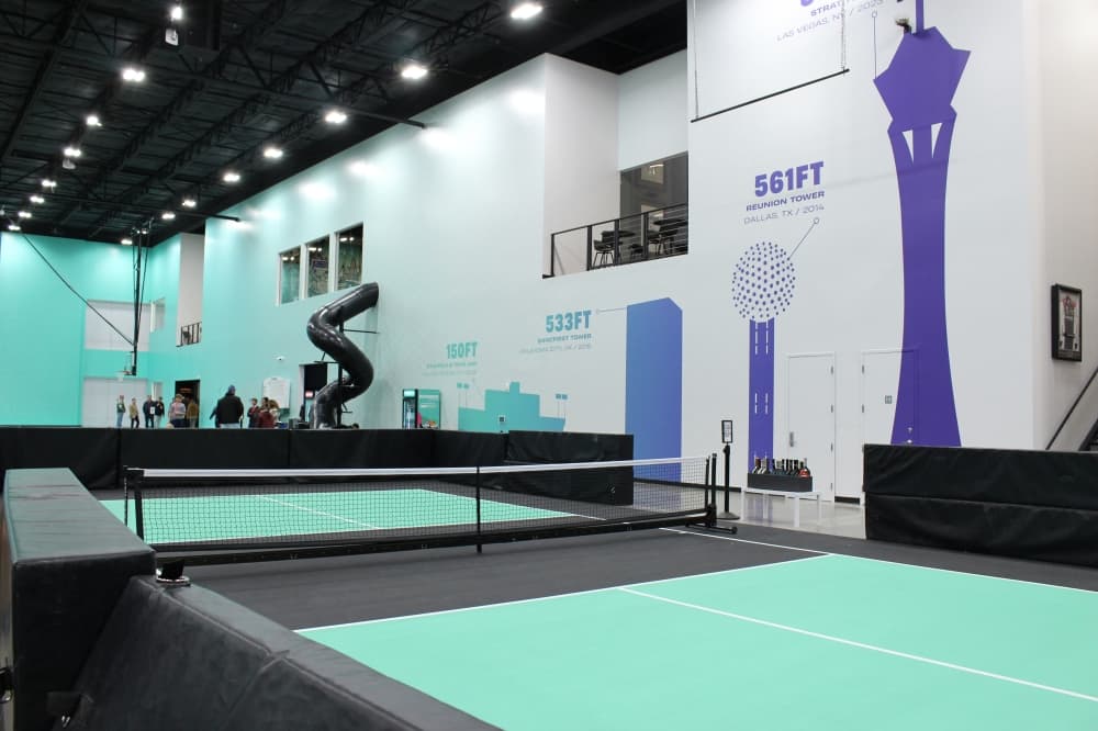 A pickleball court on the first floor of the Dude Perfect headquarters in Frisco stands next to a mural depicting the entertainment group's tallest trick shot achievements. (Alex Reece/Community Impact) 