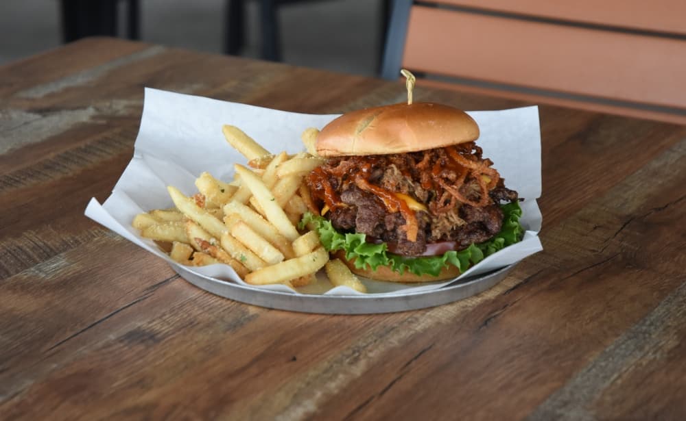 A massive burger with pulled pork and fresh ingredients rests on a platter next to Parmesian truffle fries. 