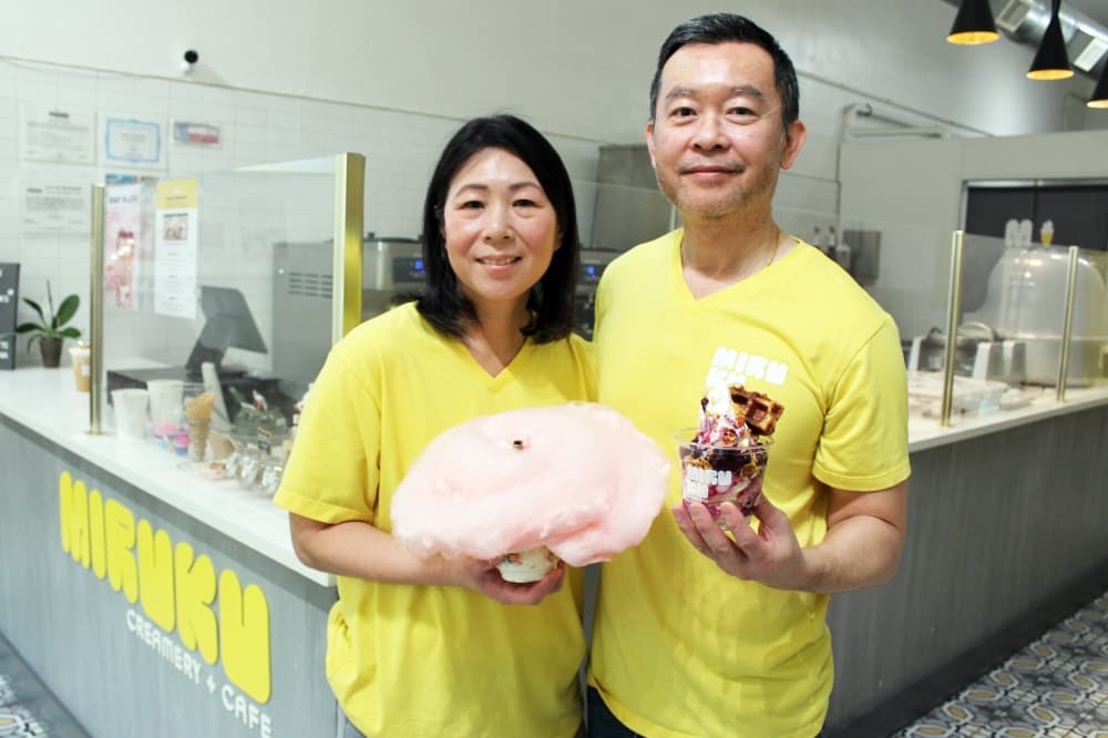 Female and male wearing yellow shirts holding ice cream and cotton candy. 