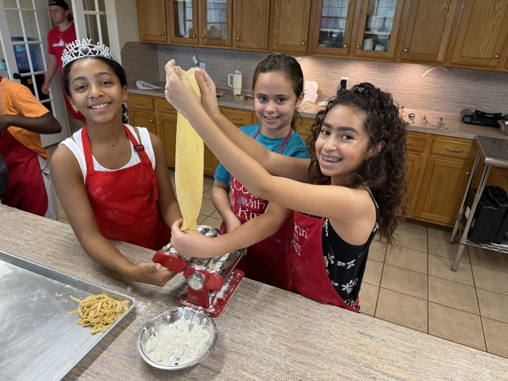 Three children pose for a photo while cooking at a Cookin' with Kim camp.