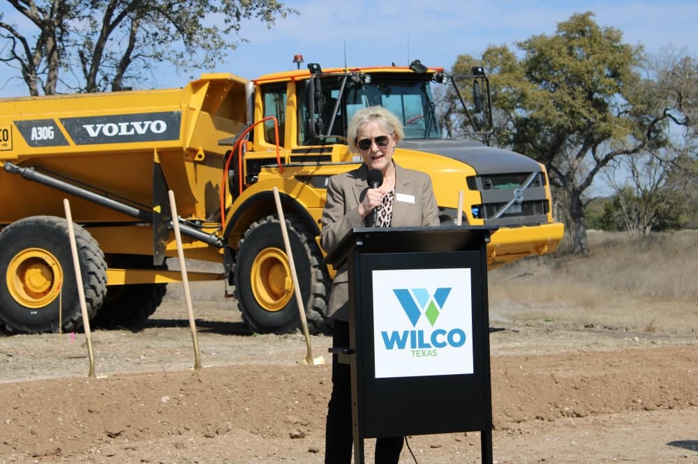 Woman stands at podium for road groundbreaking. 