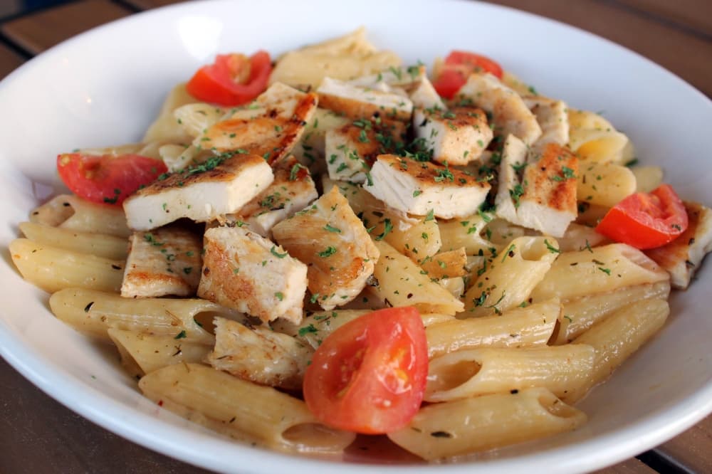 Bowl of pasta topped with chicken, cheese and tomatoes. 