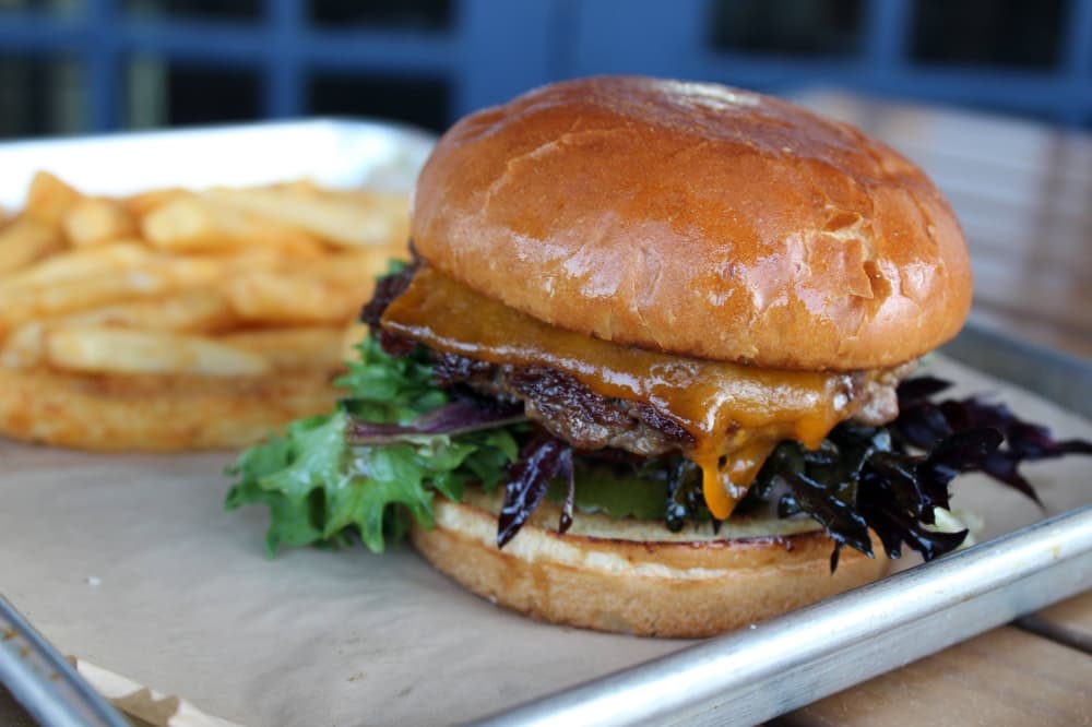 Hamburger on a paper-lined metal tray with side of fries. 