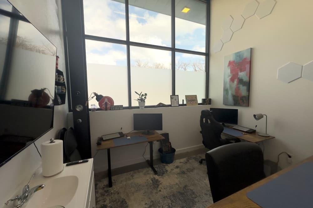 The office is shown with a big window in the back, three desks and other office supplies.