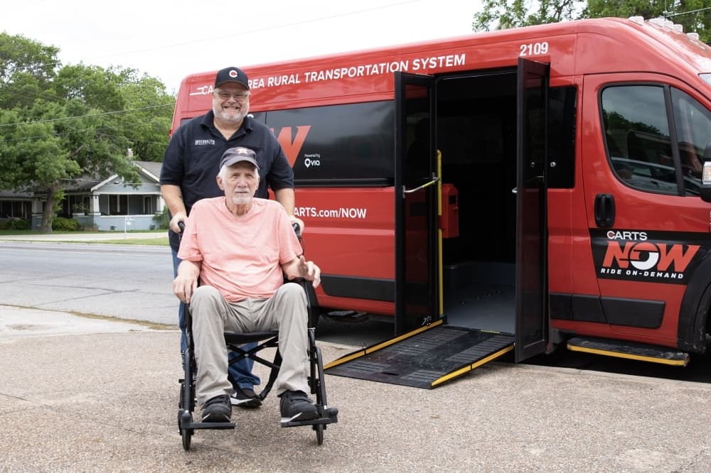 A CARTS bus driver and an elderly person in a wheelchair pose for a photo near a wheelchair-accessible CARTS vehicle.