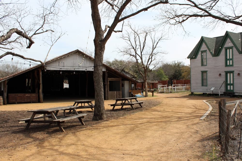 Picnic tables set on a gravel path with historic buildings nearby. 