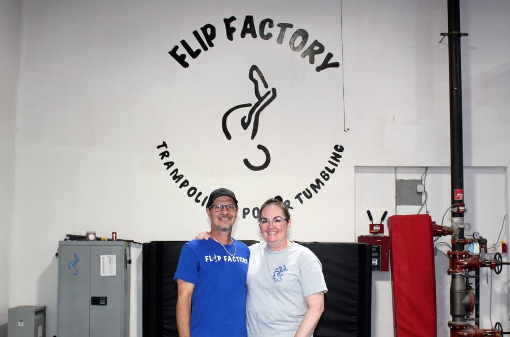 Male and female standing next to each other in front of a wall with Flip Factory signage. 