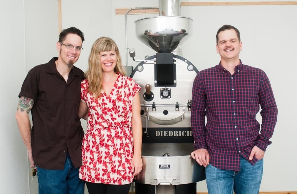 Wild Gift Coffee owners in front of an industrial sized coffee roasting machine