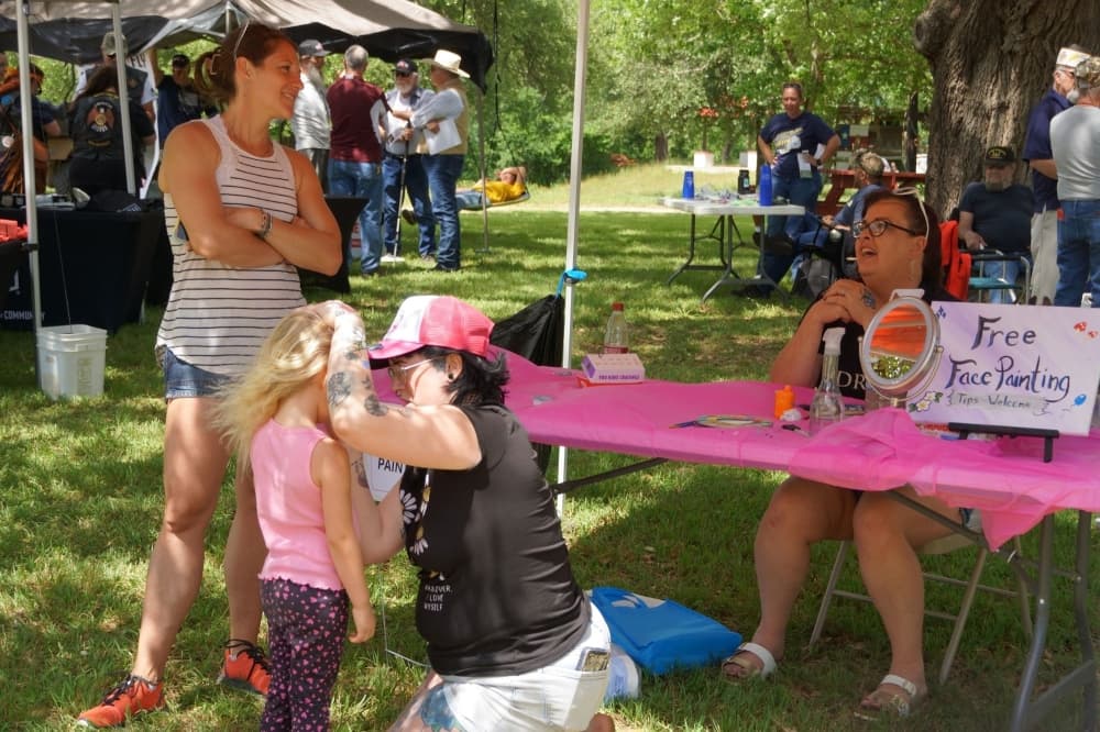 A child is getting her face painted while adults are nearby.