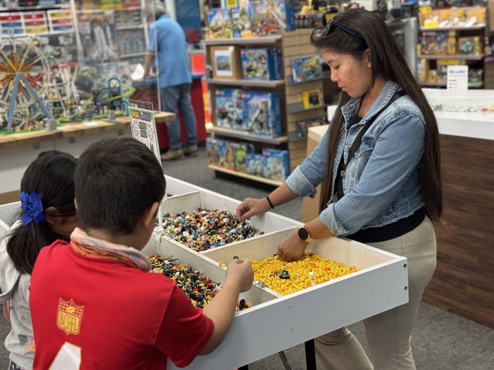Three people digging through a bin of loose LEGO