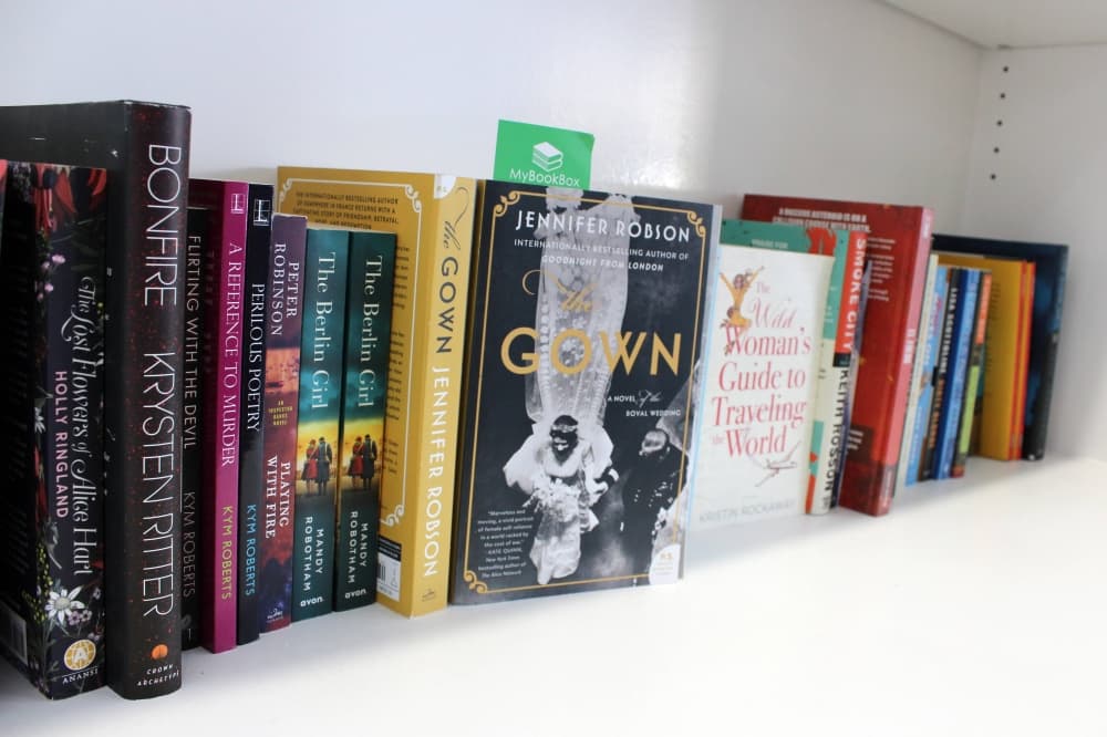 Various new paperback books on a white shelf. 