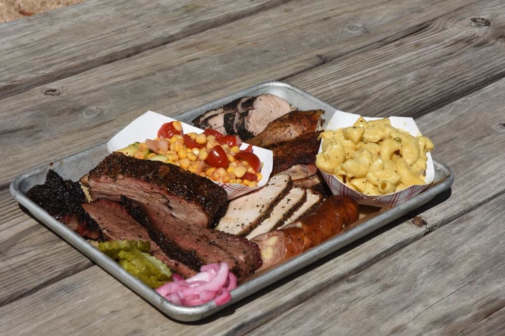 A large plate of various meats sits on a picnic table. 