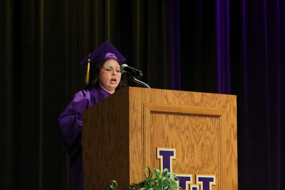 A teenage girl speaks at a podium in a cap and gown