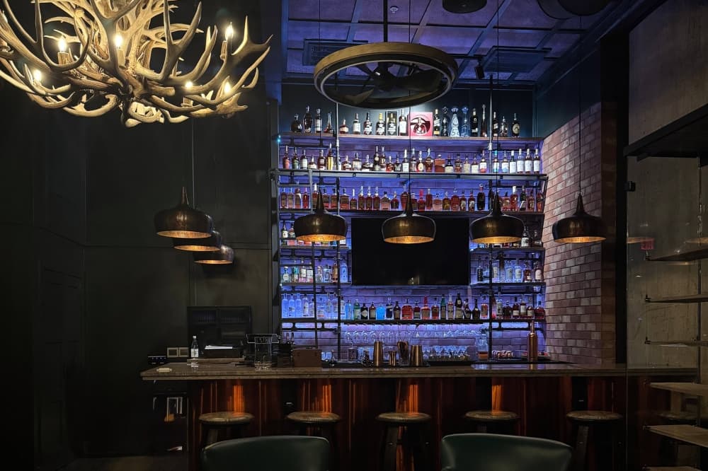 Dimly lit bar with blue light lit mirrored shelves with bottles of alcohol. 