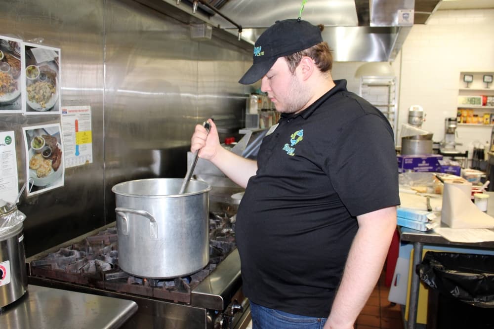 Male stirring something in a large pot sitting on an industrial stove in a restaurant kitchen. 