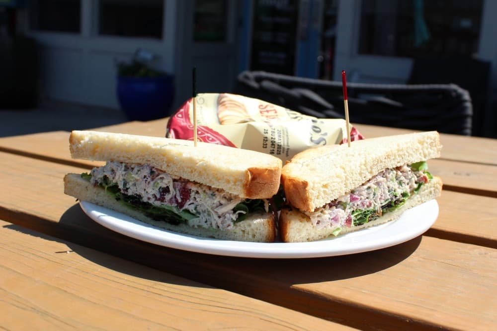 Chicken salad sandwich with a side of potato chips sitting on an outside table. 