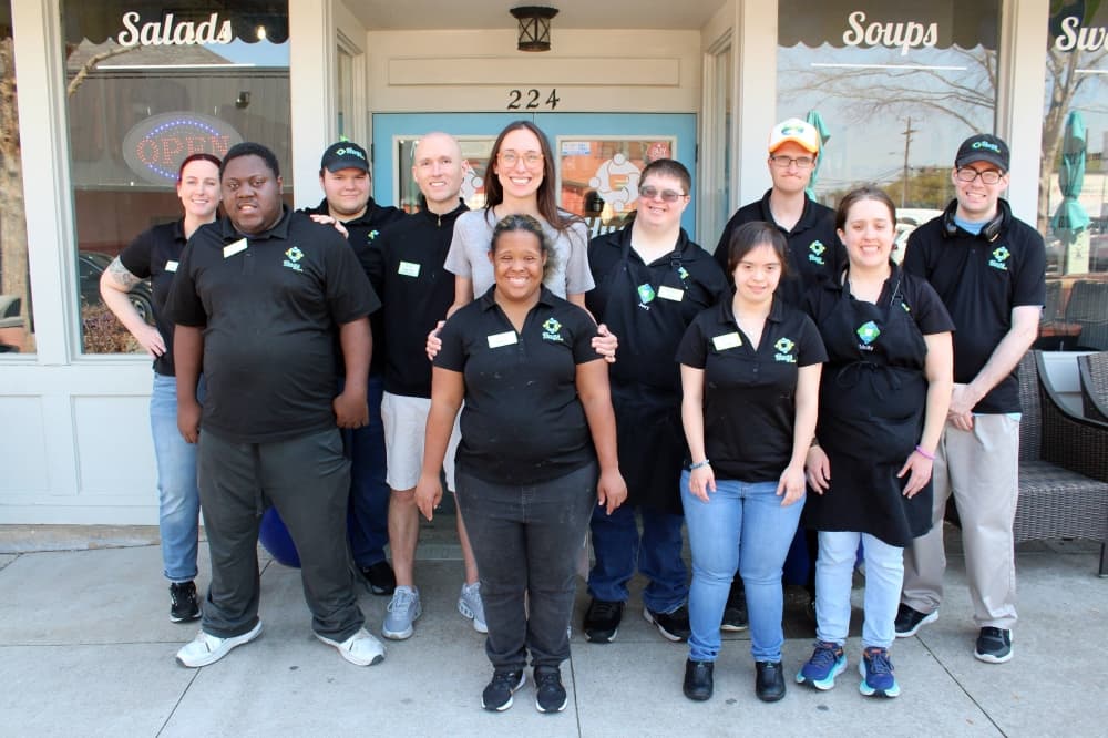 Group of males and females posed for a picture in front of a restaurant. 