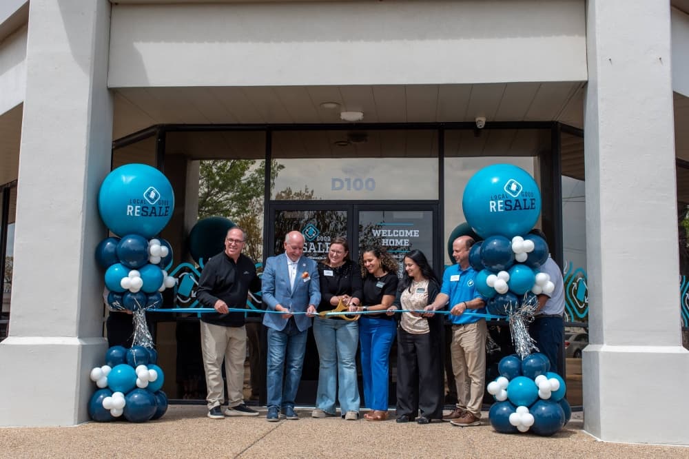 Group of people in front of.a storefront cutting a ceremonial ribbon. 