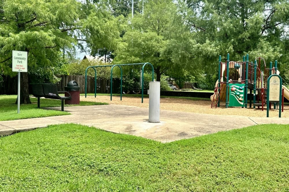 Green trees and grass surround a playground and water fountain.