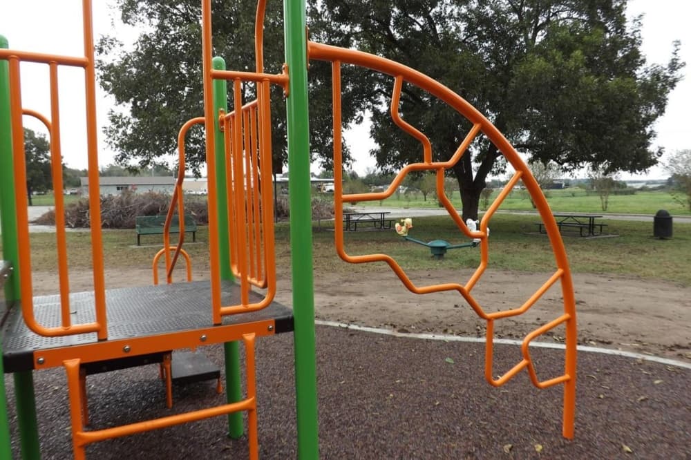 An orange and green playground is shown with trees in the background.