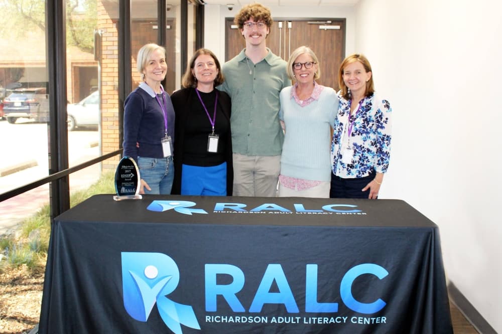 Four females flanking one male standing behind a table with RALC branded table cover. 