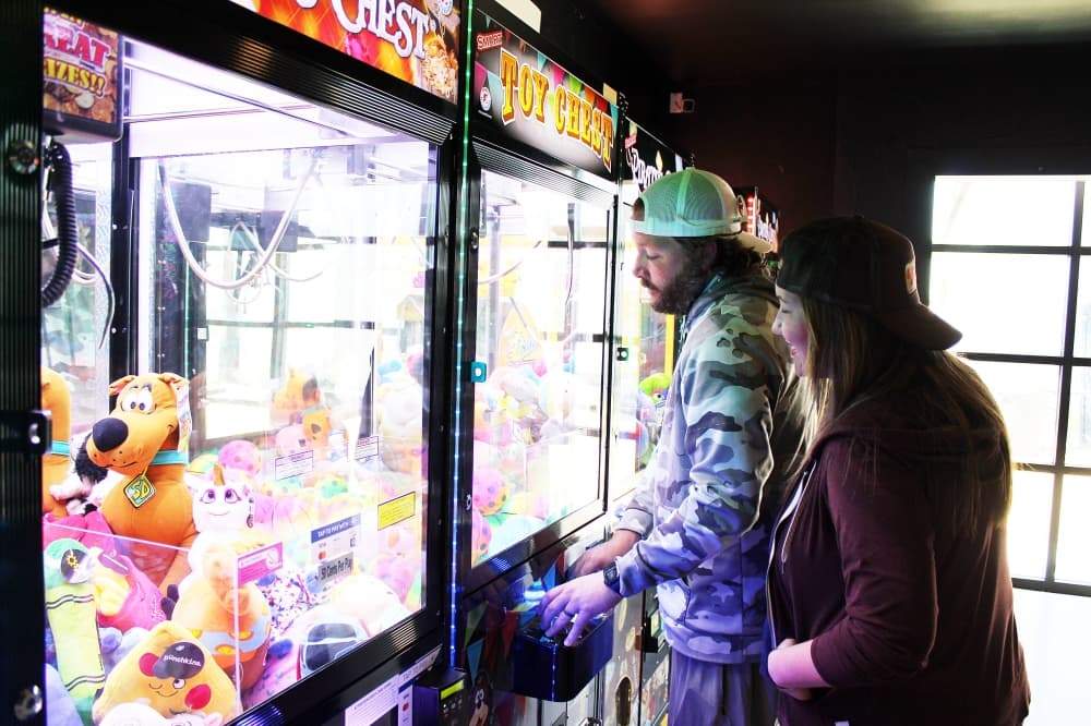 Adult male playing claw machine while adult female watches. 