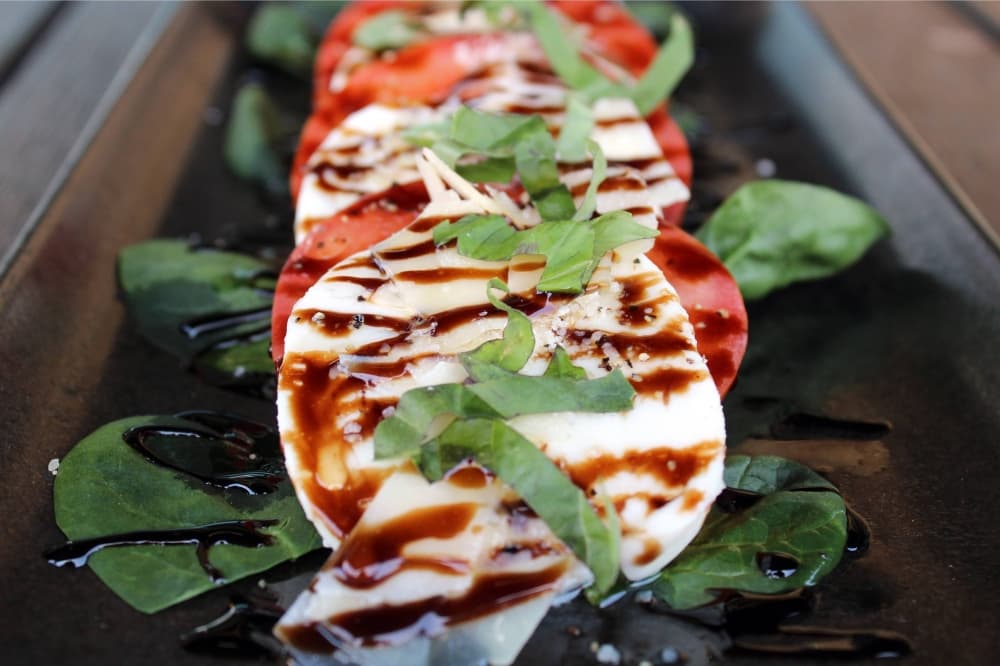 Slices of mozzarella cheese and tomatoes topped with basil, olive oil and balsamic dressing.