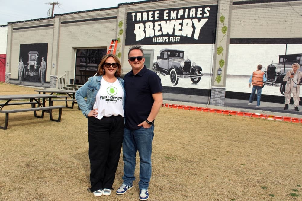 Female and male standing outside a building featuring a Three Empires Brewery mural.