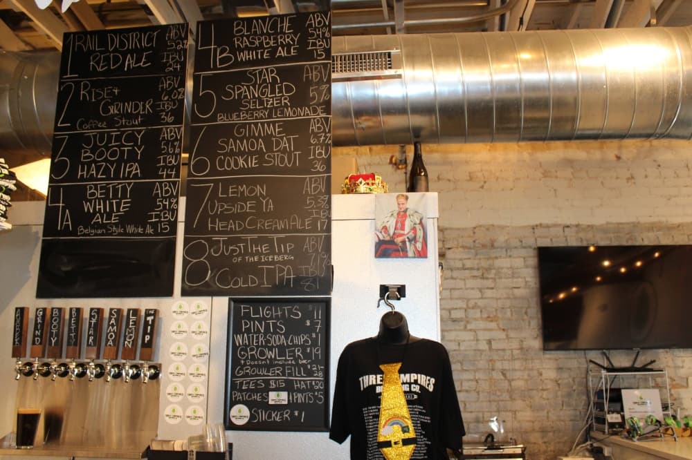 Interior of a brewery with a chalkboard menu listing different types of beer. 