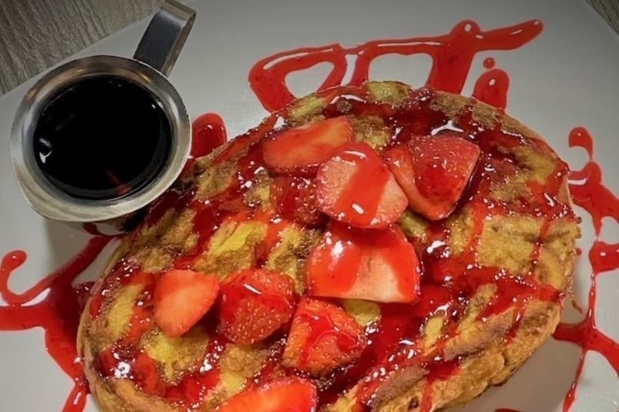 Pancakes topped with strawberries and red syrup. 