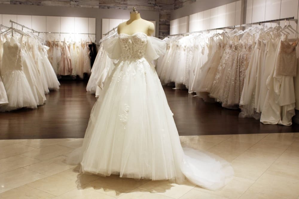 Wedding gown on a mannequin in front of aisles of wedding gowns. 