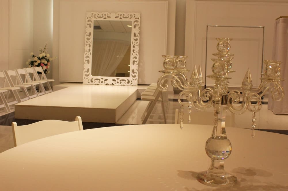 Glass candelabra on a table in front of a white runway lined with chairs. 